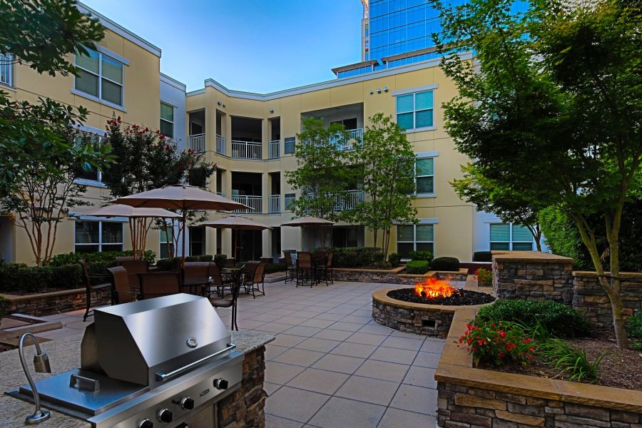 Attain Downtown East apartment homes with Apartment courtyard with a grill, patio tables, umbrellas, and a lit fire pit surrounded by trees.