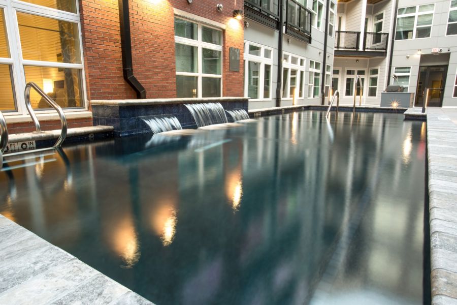 Attain Downtown apartment homes with Modern indoor pool with cascading water features, surrounded by windows and brick and white walls.