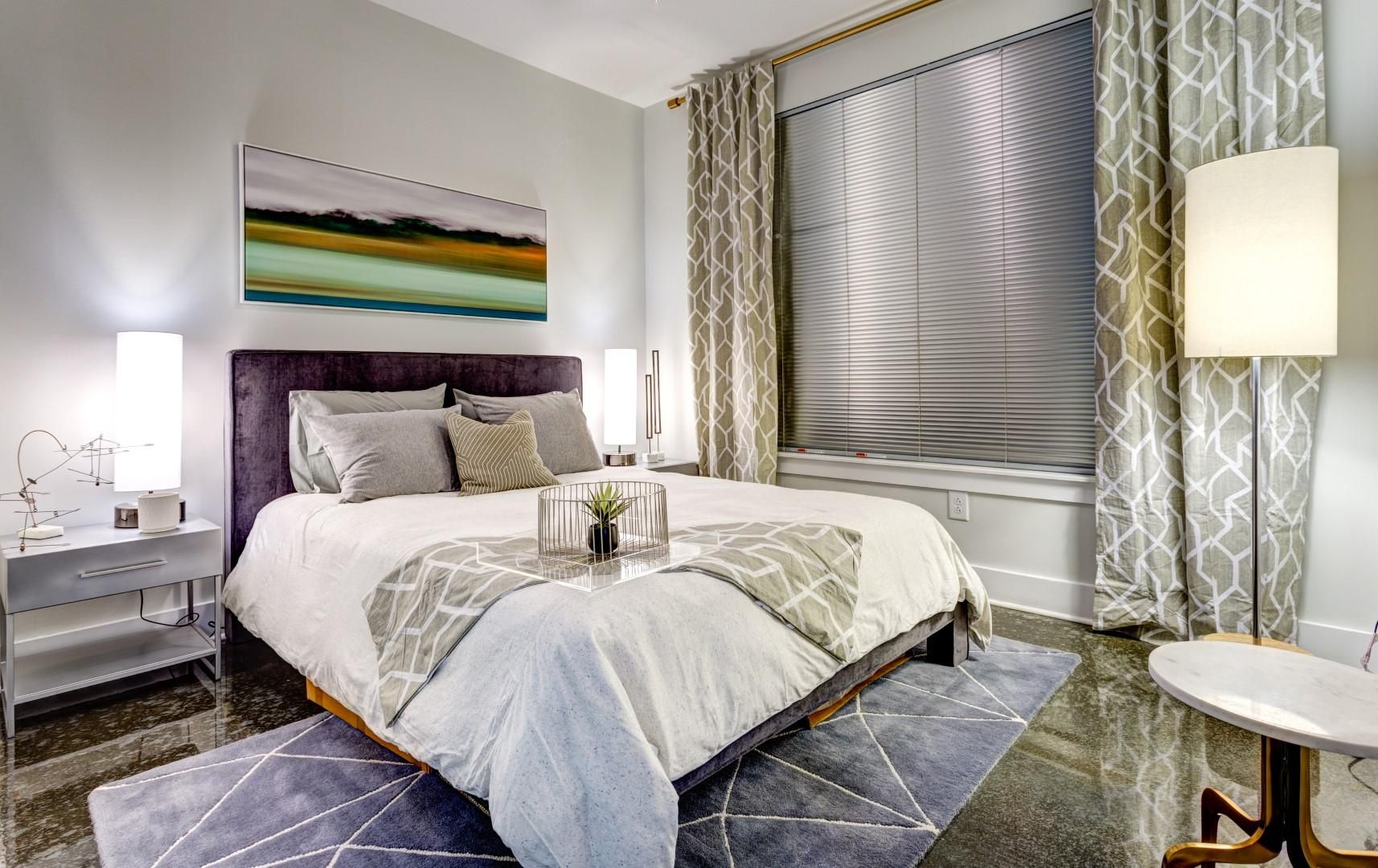 Attain Downtown apartment homes with Modern bedroom with neutral decor, double bed, large window, patterned curtains, and warm lighting.