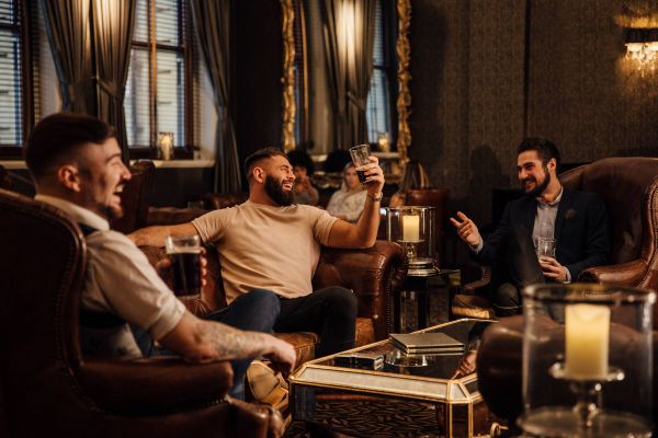 Attain on 5th apartment homes with Three men sit in leather chairs, laughing and enjoying drinks in a warmly-lit, elegant lounge.