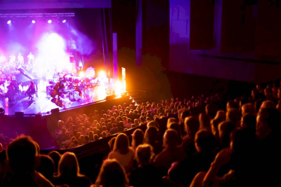 Attain Downtown apartment homes with Audience in a dark theater watching a live performance on a brightly lit stage with purple and orange lights.