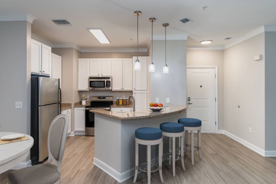 Attain Downtown East apartment homes with Modern kitchen with white cabinets, stainless steel appliances, and a curved island with three blue stools.