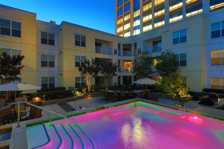 Attain Downtown East apartment homes with Colorful lights illuminate a pool in a modern apartment courtyard at dusk, with seating and plants nearby.