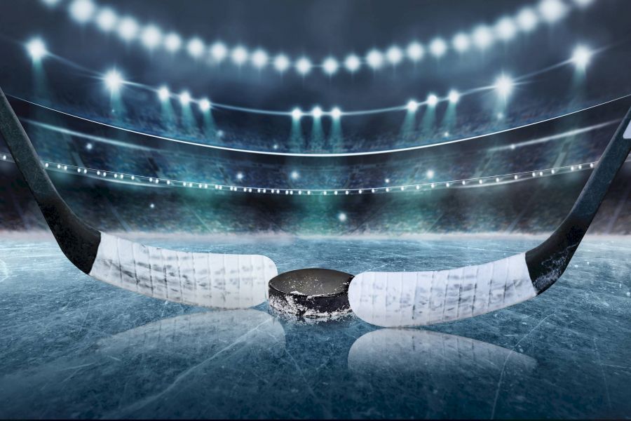 Attain Downtown apartment homes with Two hockey sticks face off over a puck on an icy rink, with stadium lights and stands in the background.