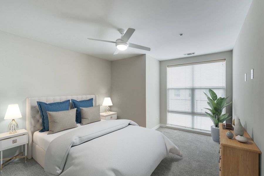 Attain Downtown East apartment homes with Modern bedroom with a white bed, blue pillows, nightstands, dresser, plant, and large window with blinds.