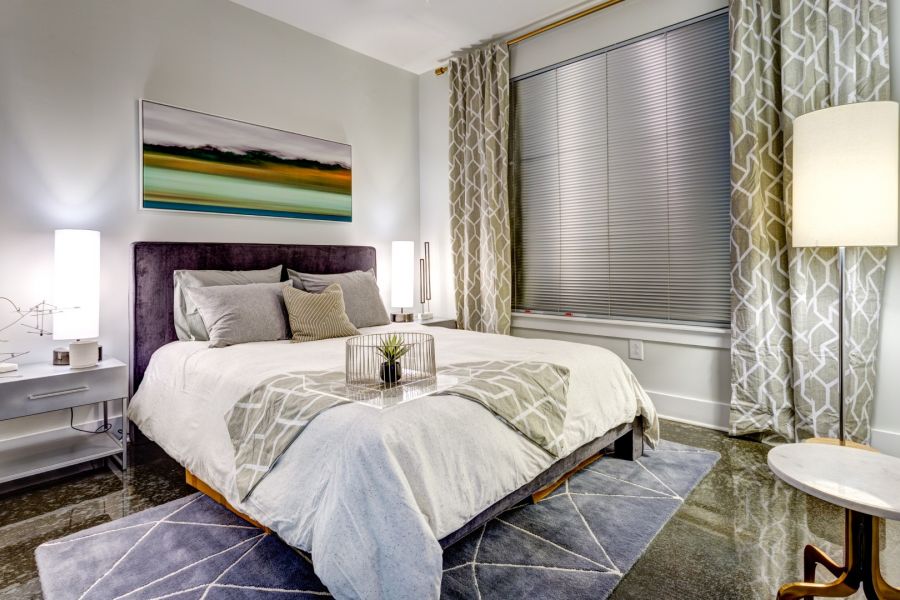 Attain Downtown apartment homes with Modern bedroom with a large bed, bedside tables, lamps, abstract art, and patterned curtains.