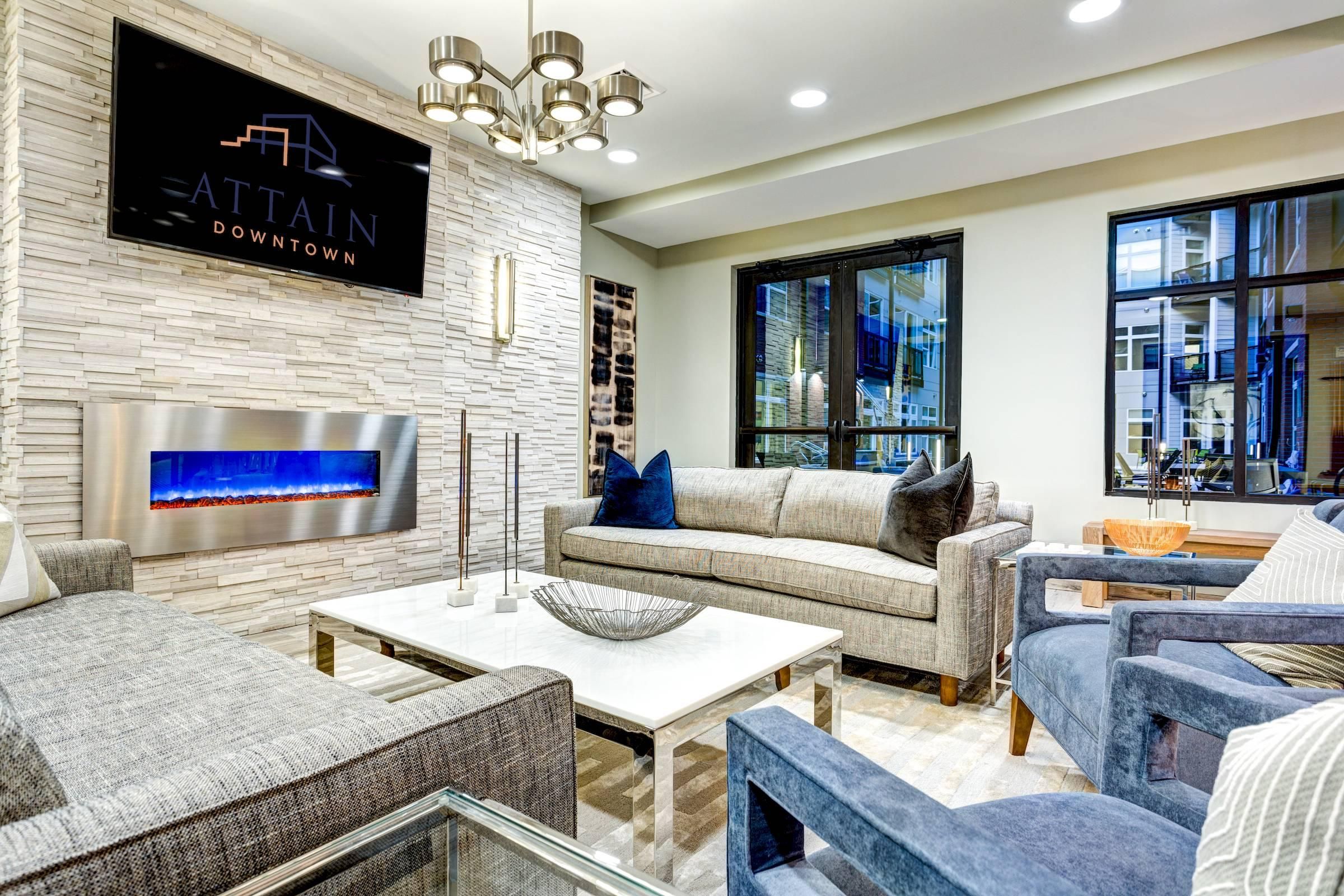 Attain Downtown apartment homes with Modern living room with grey sofas, blue chairs, a wall-mounted TV, and an electric fireplace.