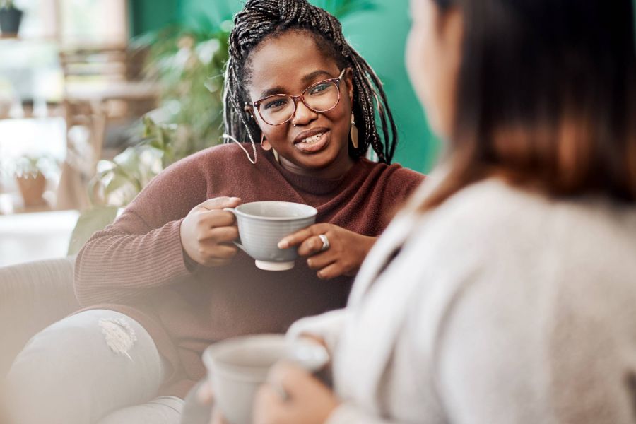 Attain on 5th apartment homes with Two women sit together, smiling and talking while holding mugs in a cozy indoor setting.