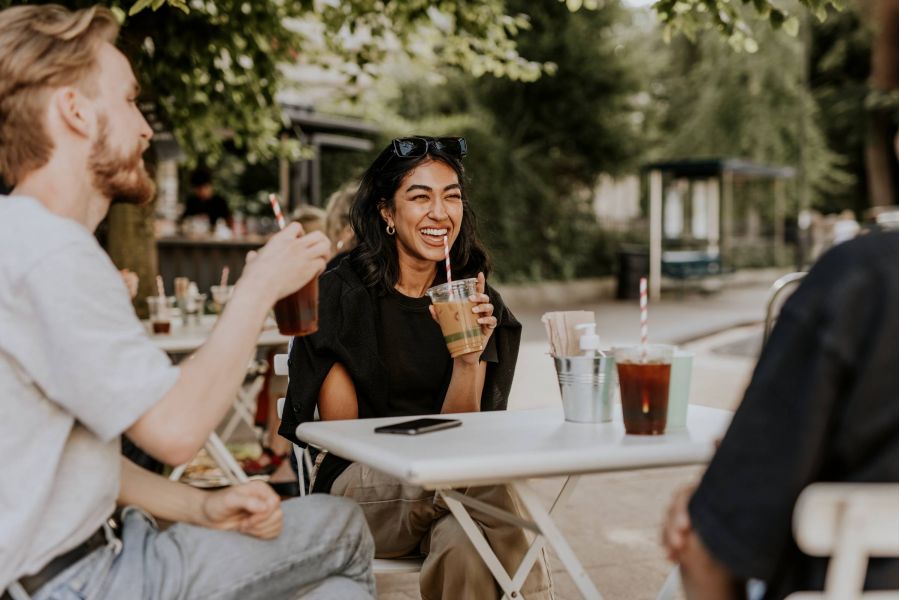 Attain on 5th apartment homes with Three friends laugh and enjoy iced drinks together at an outdoor cafe on a sunny day.