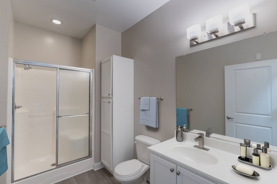 Attain Downtown East apartment homes with Modern bathroom with a glass shower, white cabinets, sink, toilet, and large mirror above the vanity.