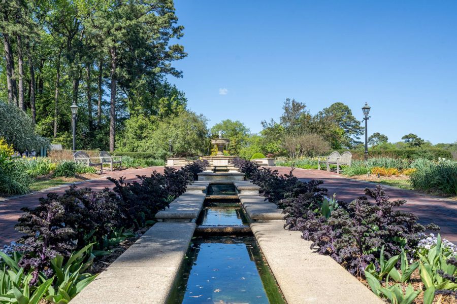 Attain Downtown apartment homes with a view of Norfolk Botanical Garden with a water feature leading to a fountain, with benches and trees under a clear blue sky.