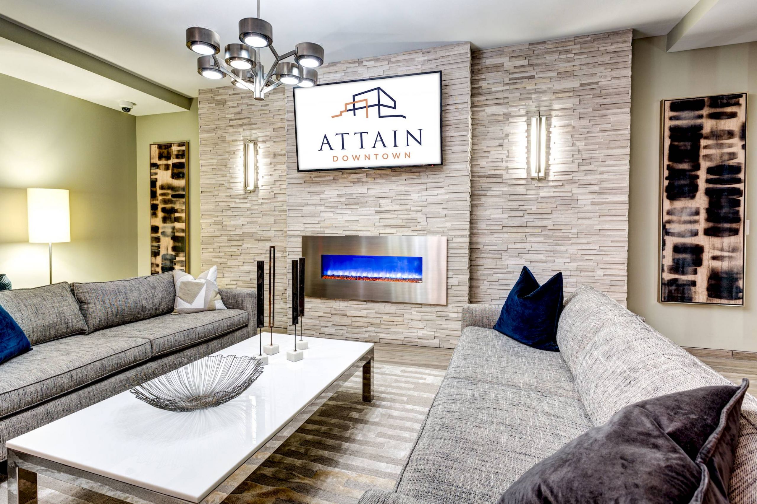 Attain Downtown apartment homes with Modern living room with gray sofas, a white coffee table, and a fireplace below a TV displaying "Attain Downtown.