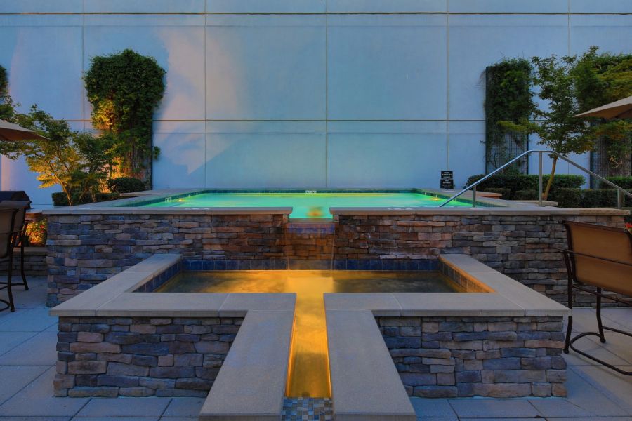 Attain Downtown East apartment homes with A glowing pool with stone walls and water features, set against a modern building with greenery.