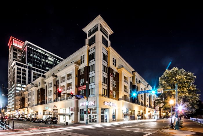 Attain Downtown East apartment homes with Night view of a modern city intersection with lit shops and apartment buildings, streets empty of people.