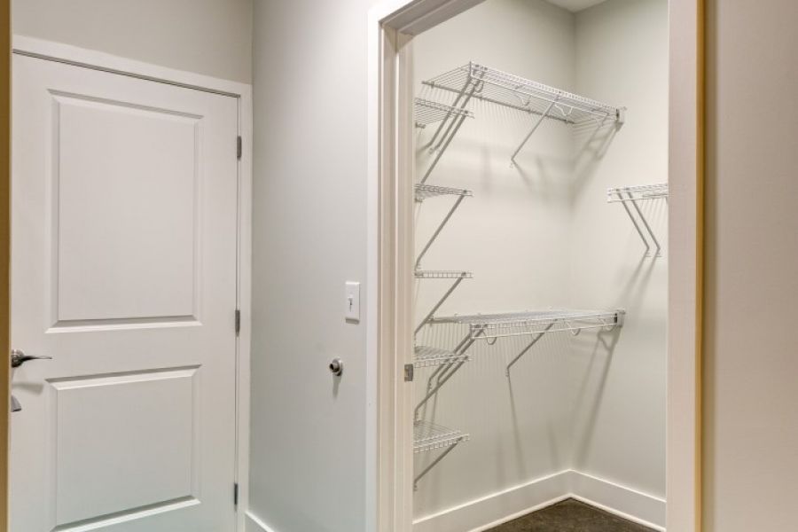 Attain Downtown apartment homes with A small empty walk-in closet with wire shelves and a teal rug outside the door.