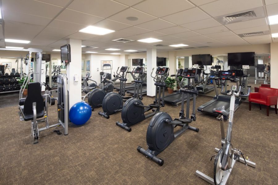 Attain Downtown East apartment homes with A gym with cardio machines, weight equipment, a blue exercise ball, and red chairs in the corner.
