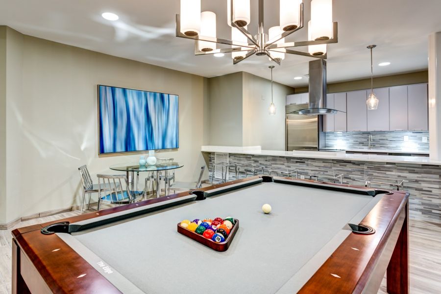 Attain Downtown apartment homes with Modern game room with a gray pool table, kitchen bar, dining table, and abstract wall art.