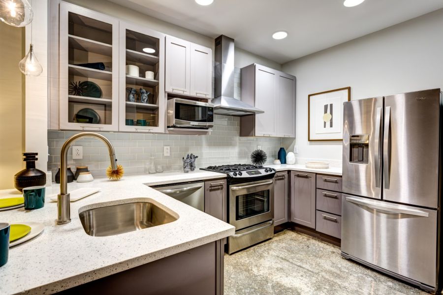 Attain Downtown apartment homes with Modern kitchen with stainless steel appliances, white countertops, and gray cabinets under bright lighting.
