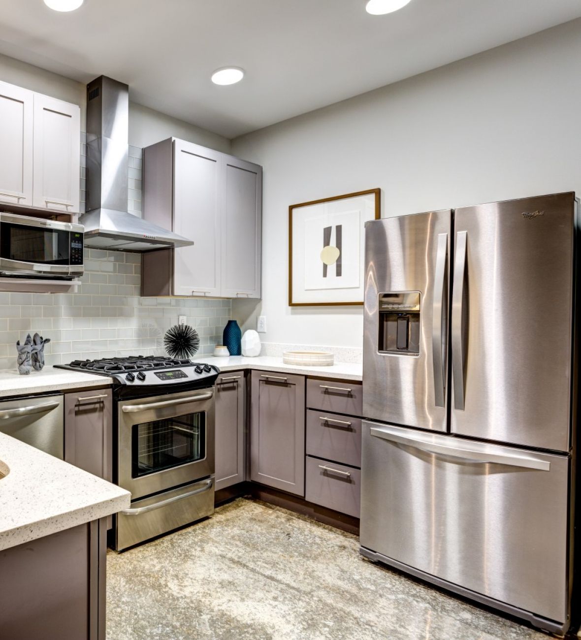 Attain Downtown apartment homes with Modern kitchen with stainless steel appliances, white countertops, and gray cabinets under bright lighting.