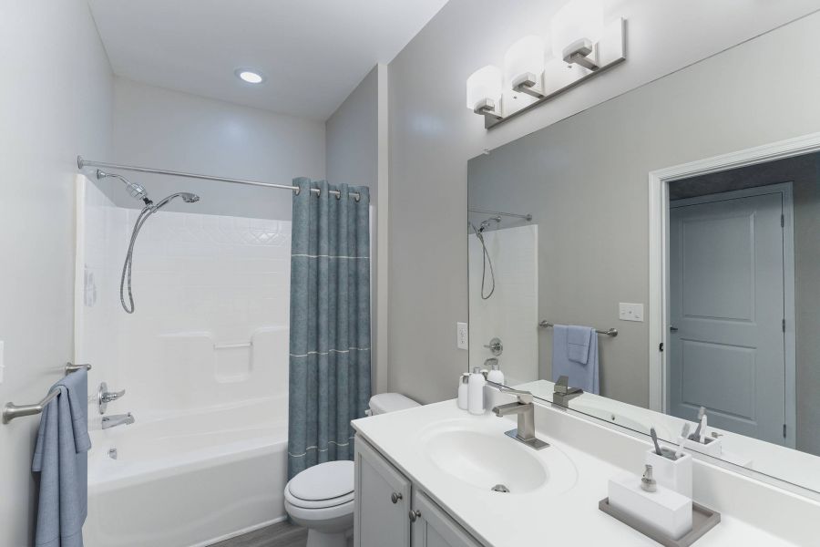 Attain Downtown East apartment homes with Modern bathroom with white fixtures, a bathtub with blue shower curtain, and a large mirror above the sink.