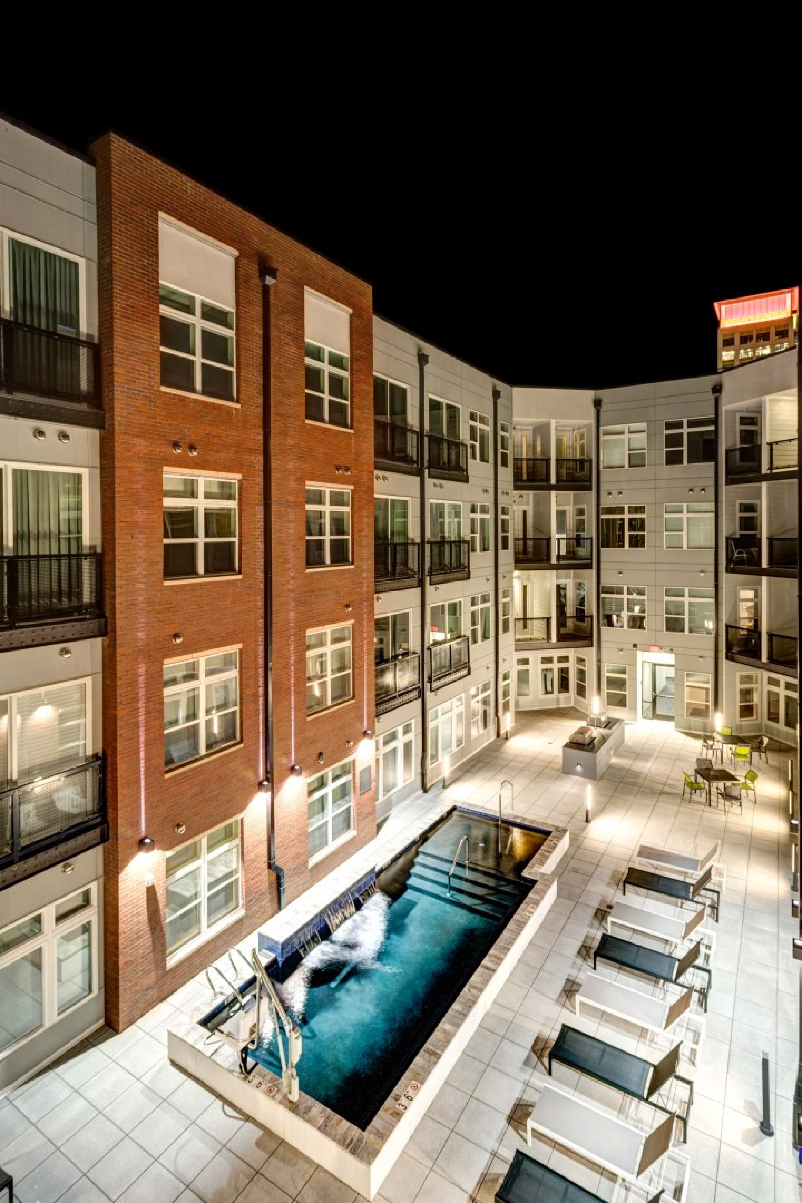 Attain Downtown apartment homes with Modern apartment complex at night with a lit pool, lounge chairs, and balconies facing the courtyard.