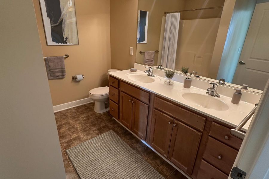 Attain Downtown apartment homes with Modern bathroom with double sinks, wood cabinets, wall art, and a textured rug on tiled floor.
