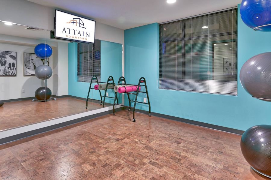 Attain Downtown apartment homes with Exercise room with yoga balls, balance bars, wall mirror, and a sign reading "ATTAIN DOWNTOWN" above the mirror.